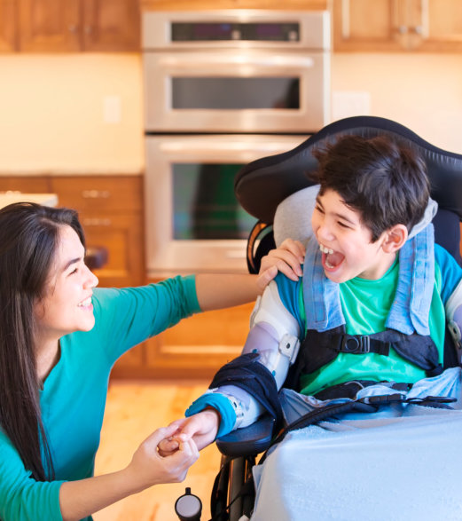 Disabled boy in wheelchair laughing with teen sister in kitchen